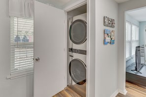 A laundry room with two stacked front-loading washers and dryers, a door leading to a balcony, and a wall with decorative items.
