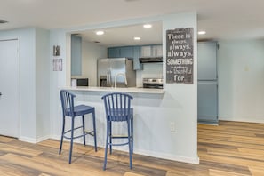 A modern kitchen with blue cabinets, stainless steel appliances, and a bar area with two stools.