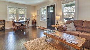 A living room with a wooden coffee table, a brown sofa, and a dining area with wooden chairs and a table. - Walk to Fox River Grove Station: Home w/ Hot Tub (Fox River Grove)