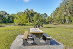 A picnic table with benches in a park with trees and grass. - Steps to Orange Lake: Pet-friendly Getaway! (Hawthorne)