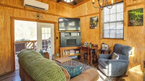 A cozy living room with wooden walls, a ceiling fan, a flat-screen TV, a comfortable sofa, and a dining area with a table and chairs. - Private Hot Tub, Deck & Mtn Views! Hickman Retreat (Hickman)