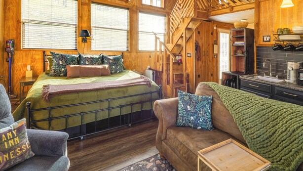 A cozy wooden cabin interior with a bed, a sofa, a staircase, and a kitchen area. - Private Hot Tub, Deck & Mtn Views! Hickman Retreat (Hickman)