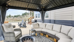 Eine überdachte Terrasse im Freien mit einer Eckcouch, Korbstühlen, einer Feuerstelle und Grillplatz.