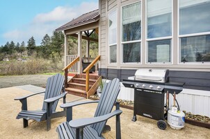 Una casa con porche, una parrilla y sillones Adirondack.