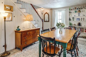 Une salle à manger avec une table en bois, des chaises, un escalier, une commode et une bibliothèque contenant divers objets.