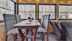 A wooden table with wicker chairs, large windows, and string lights. - Peaceful Nature Retreat w/ Hot Tub in Eastern WV! (Lost River)