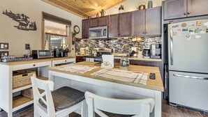 A modern kitchen with wooden cabinets, a stainless steel refrigerator, and a central island with seating. - Peaceful Nature Retreat w/ Hot Tub in Eastern WV! (Lost River)