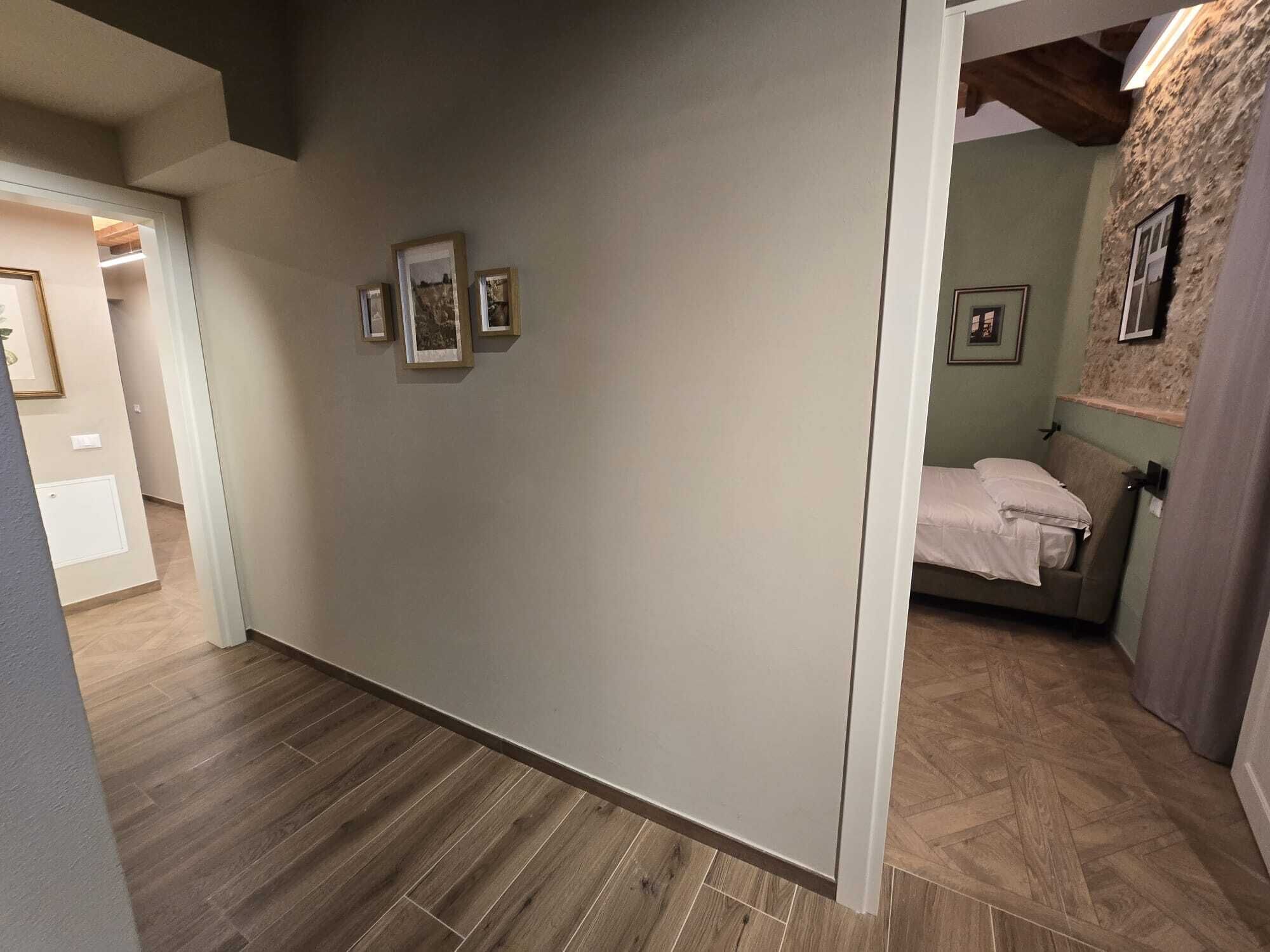 Un couloir avec un plancher en bois, un lit recouvert d’une courtepointe blanche et un mur orné de tableaux encadrés.