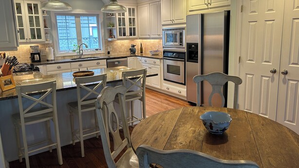A modern kitchen with white cabinetry, stainless steel appliances, and a wooden dining table. - In-town Lewes house with great floor plan!  112 Bradley Lane (Lewes)