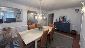 A dining area with a white table, wicker chairs, and a chandelier. There is a blue cabinet with decorative items on top. - In-town Lewes house with great floor plan!  112 Bradley Lane (Lewes)