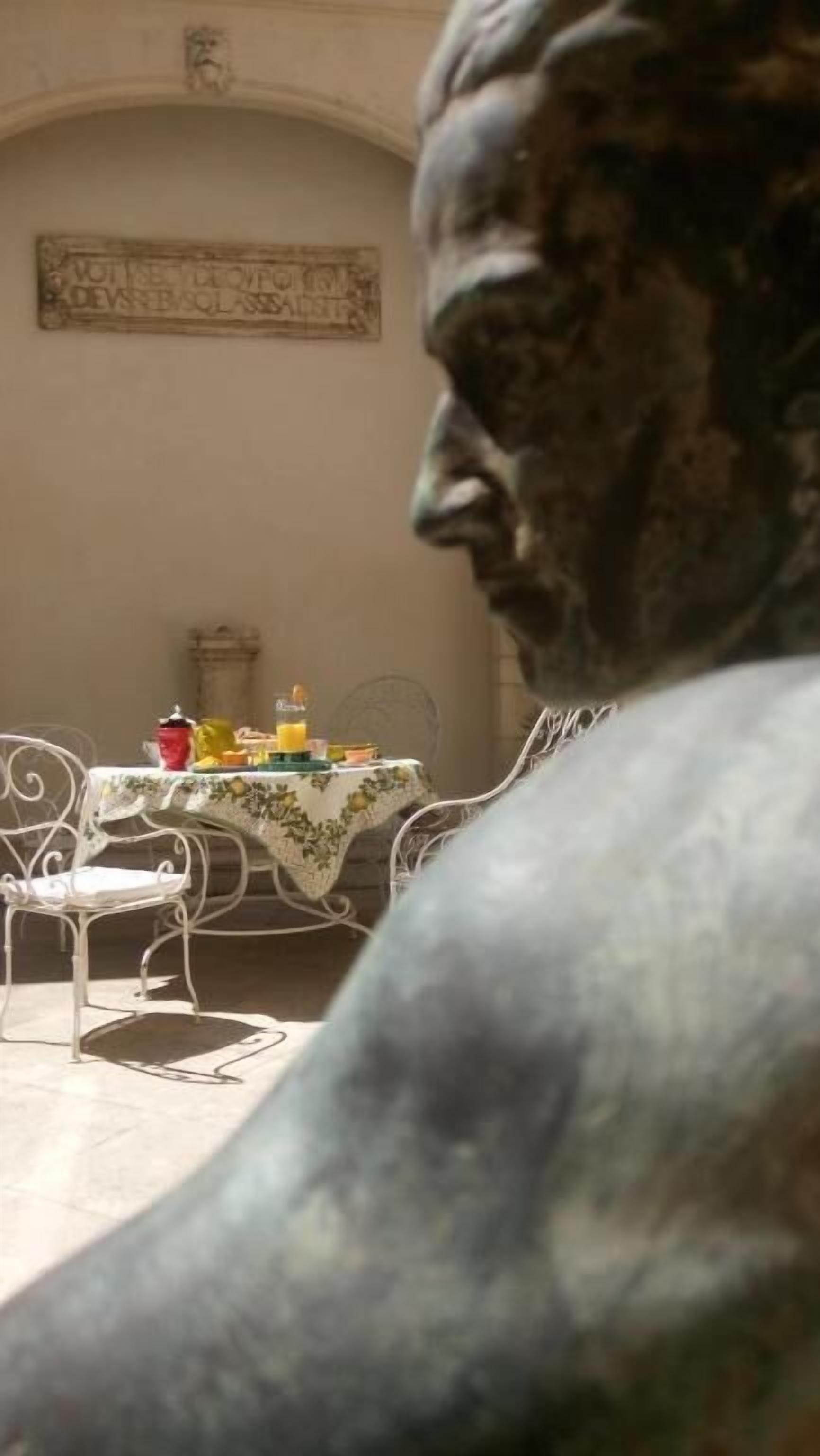 A statue in a dining area with a table set for two, featuring a red pot and a yellow jug.