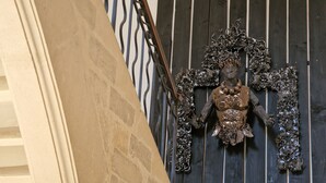 Une sculpture décorative en métal aux motifs complexes, fixée sur un panneau en bois foncé orné de lignes verticales.