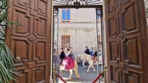 Une porte en bois ornée de sculptures complexes, qui donne sur une scène de rue animée, avec des gens et des chevaux.
