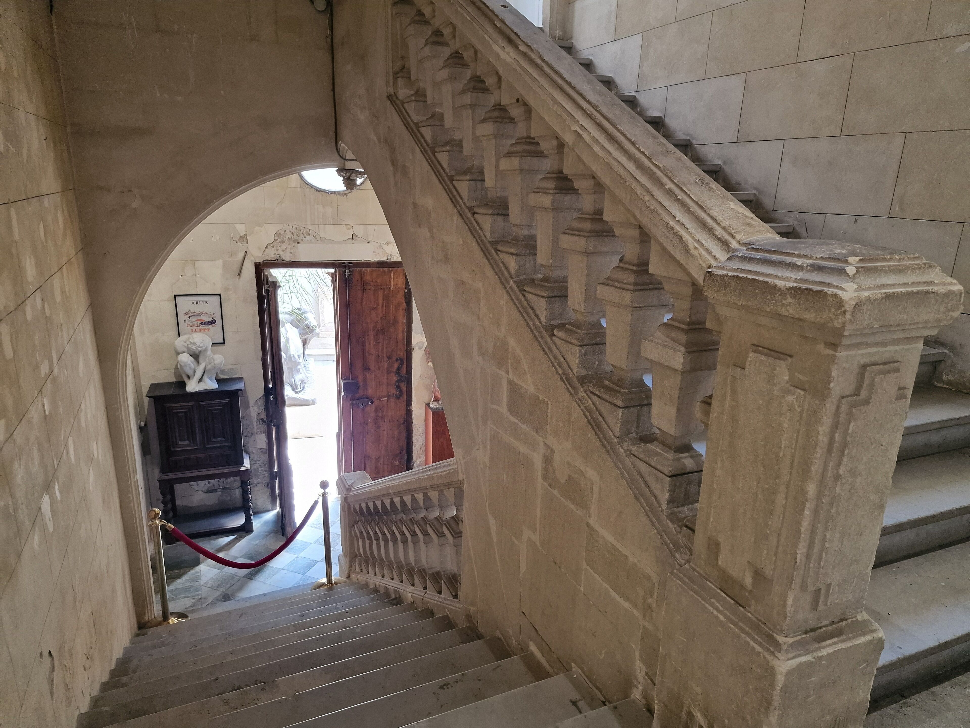 A stone staircase with a red rope barrier, leading to a doorway with a wooden door and a framed picture above it.
