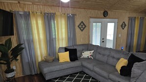 Sala de estar com sofá modular cinza, tapete xadrez preto e branco e planta em vaso.