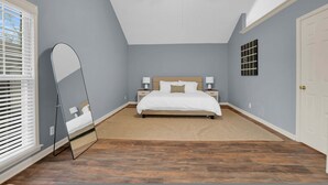Une chambre à coucher avec un lit, un ventilateur de plafond, un grand miroir et une fenêtre avec des stores.