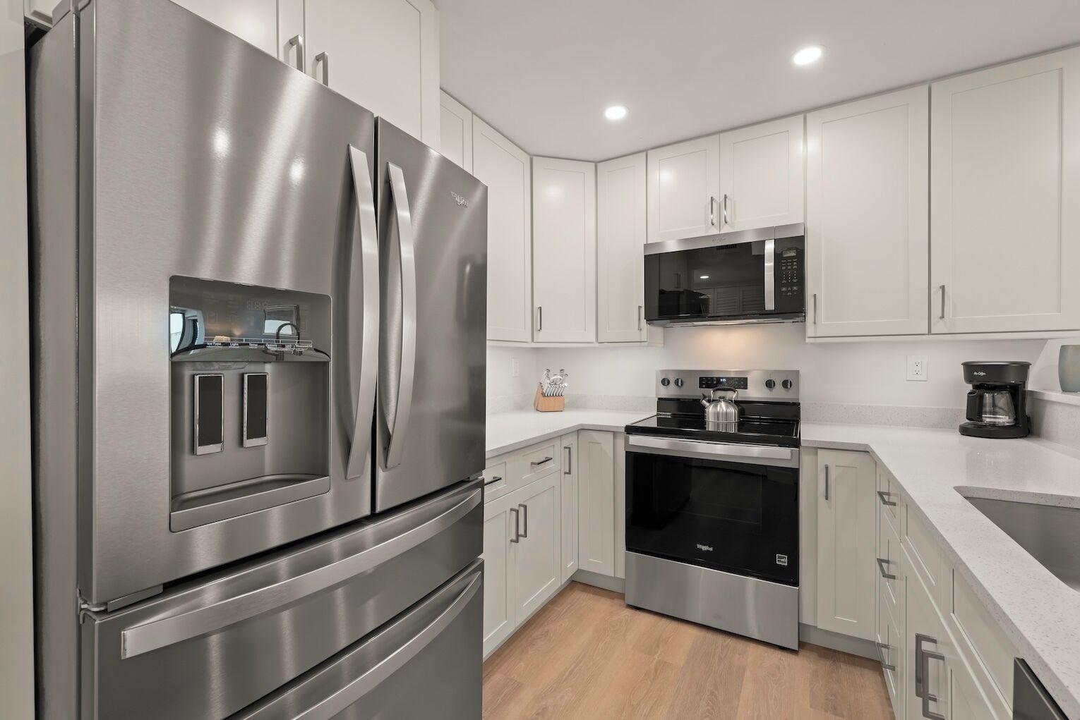 A modern kitchen with stainless steel appliances, white cabinetry, and a built-in oven.