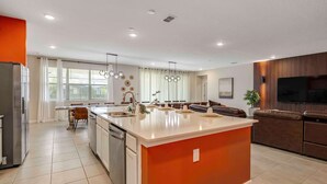 A modern kitchen with a large island, a dining area, and a living space with a TV and seating. - NBA Dream Mansion 15br Luxury Villa w Pool (Kissimmee)