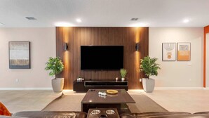A modern living room with a flat-screen TV, leather sofas, a coffee table, and two potted plants. - NBA Dream Mansion 15br Luxury Villa w Pool (Kissimmee)