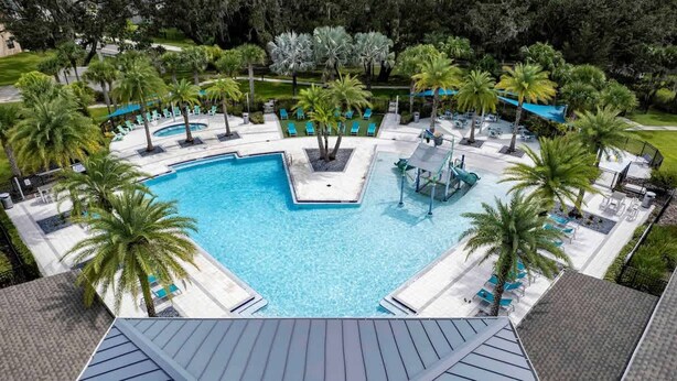 A large rectangular pool with a central island, surrounded by palm trees and lounge chairs. - NBA Dream Mansion 15br Luxury Villa w Pool (Kissimmee)