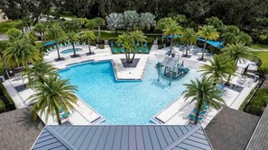 Una piscina rectangular grande con una isla central, rodeada de palmeras y sillas de descanso.