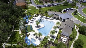 Ovenudblik over et boligområde med en swimmingpool omgivet af palmer og liggestole.