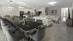 A modern living room with a dining area, white sofas, a coffee table, and a TV. - Magical 15br Villa w Pool Cinema Themed Fun (Kissimmee)