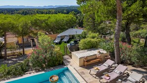 A pool area with lounge chairs and a barbecue area, surrounded by lush greenery and a view of distant mountains. - Mas Noves - Horizon Alpilles Villa (Noves)