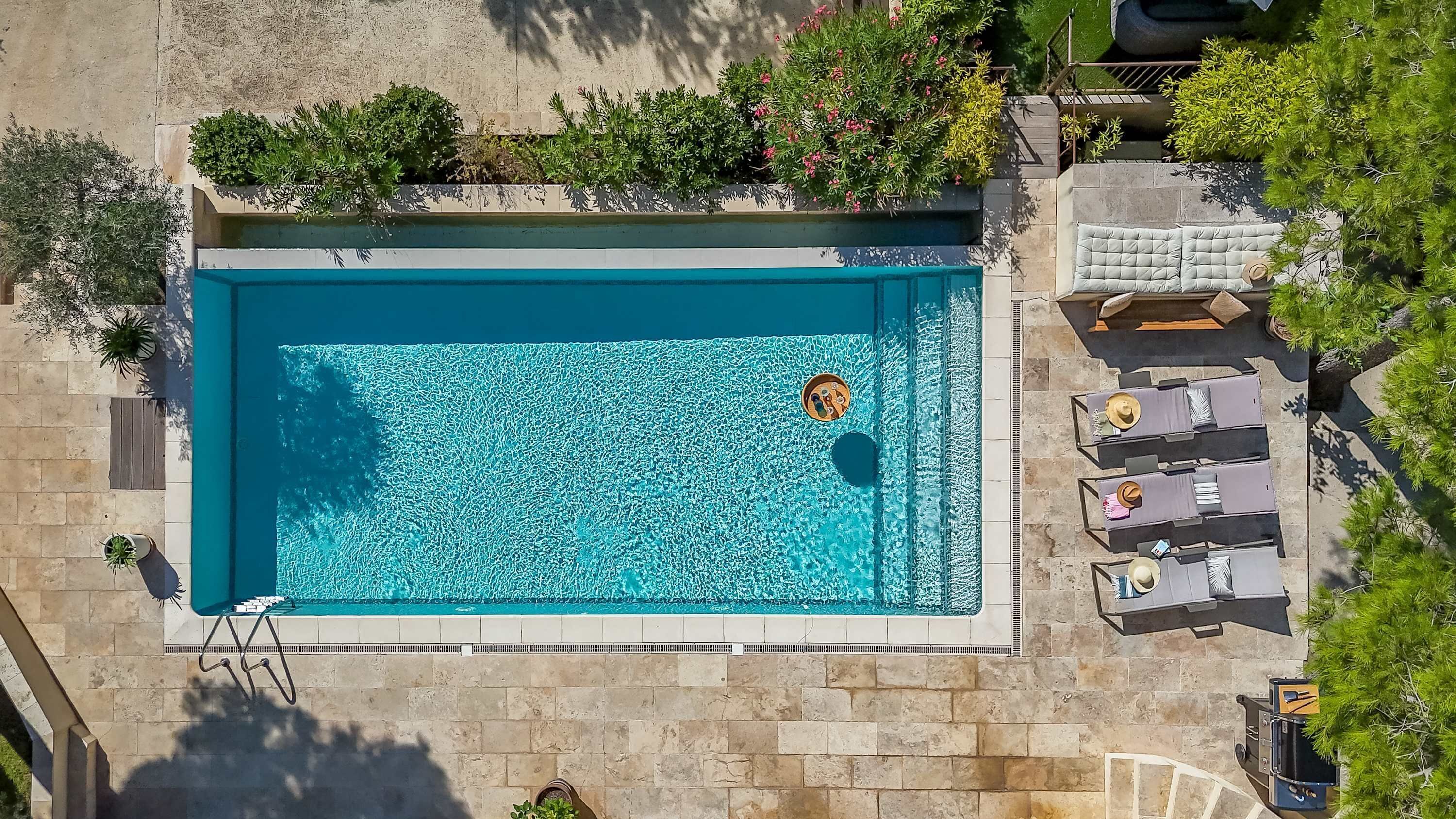 An aerial view of a rectangular swimming pool with a single lounge chair and a sun lounger.