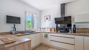 A modern kitchen with a flat-screen TV, a coffee machine, and a large window. - Mas Noves - Horizon Alpilles Villa (Noves)