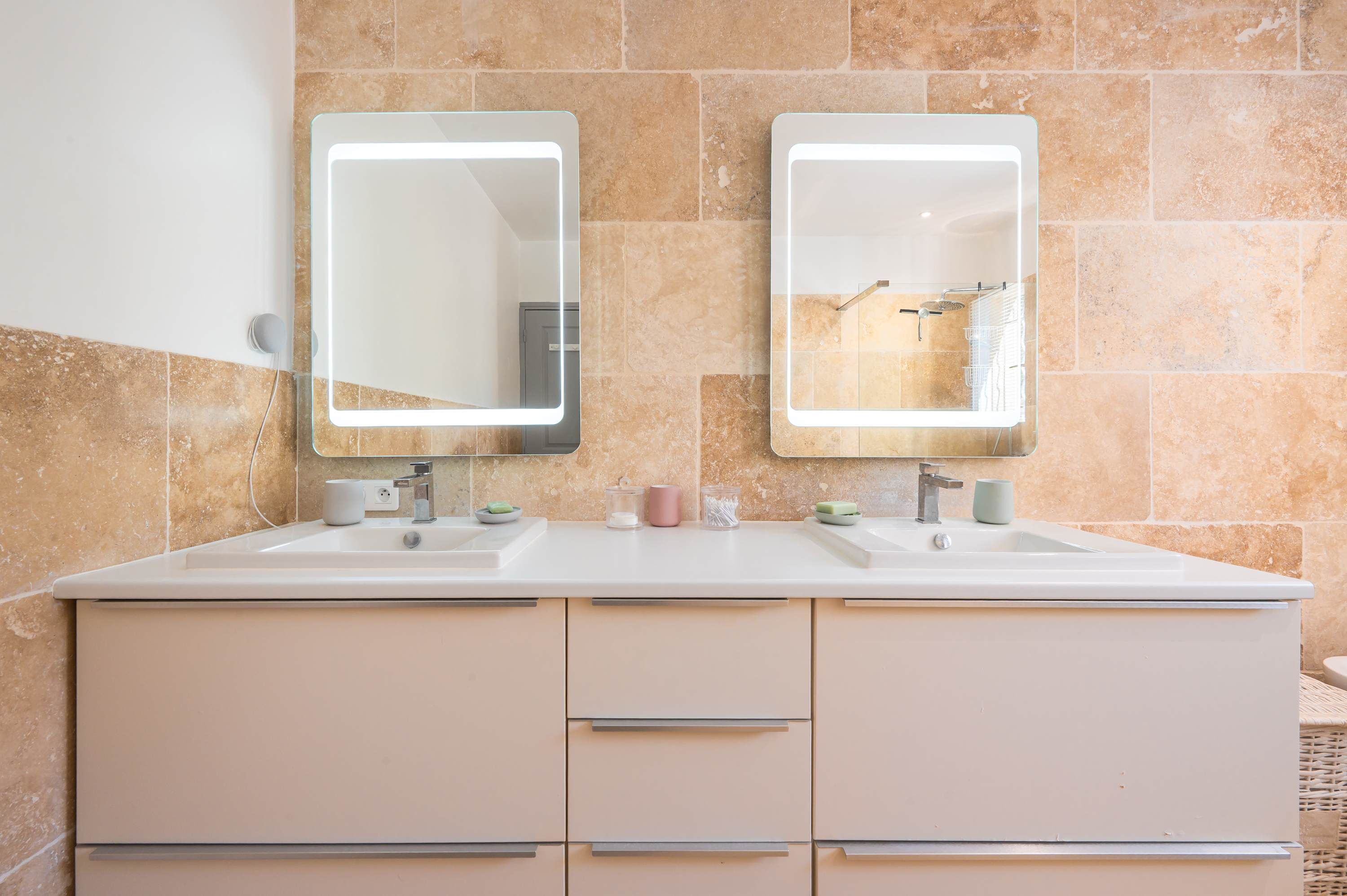 A bathroom with two sinks, each with a mirror and a faucet. There are two drawers below the sinks.