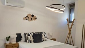 A modern bedroom with a bed, bedside tables, a wall-mounted air conditioner, a unique wall decoration, and a pendant light. - Green Residence (Hersonissos)