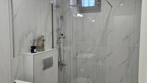 A modern bathroom with a glass-enclosed shower, a white toilet, and a marble backsplash. - Green Residence (Hersonissos)
