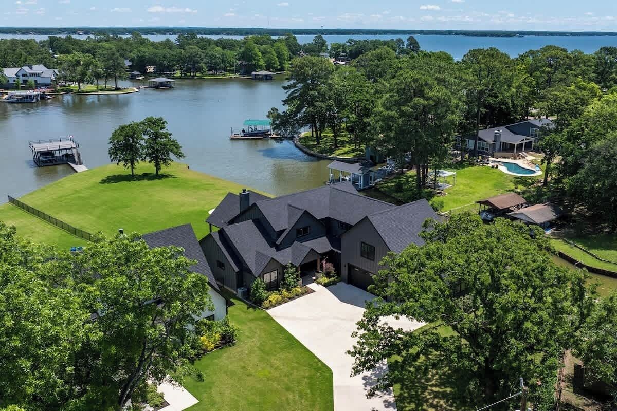 A large house with a driveway, a swimming pool, and a dock extending into a lake.