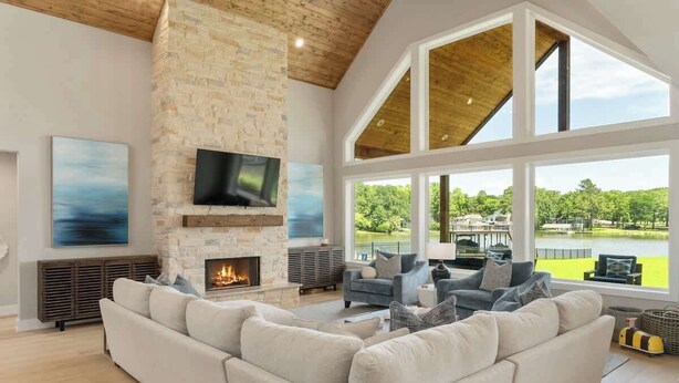 Amplia sala de estar con chimenea de piedra, ventanas grandes y vista a un lago.