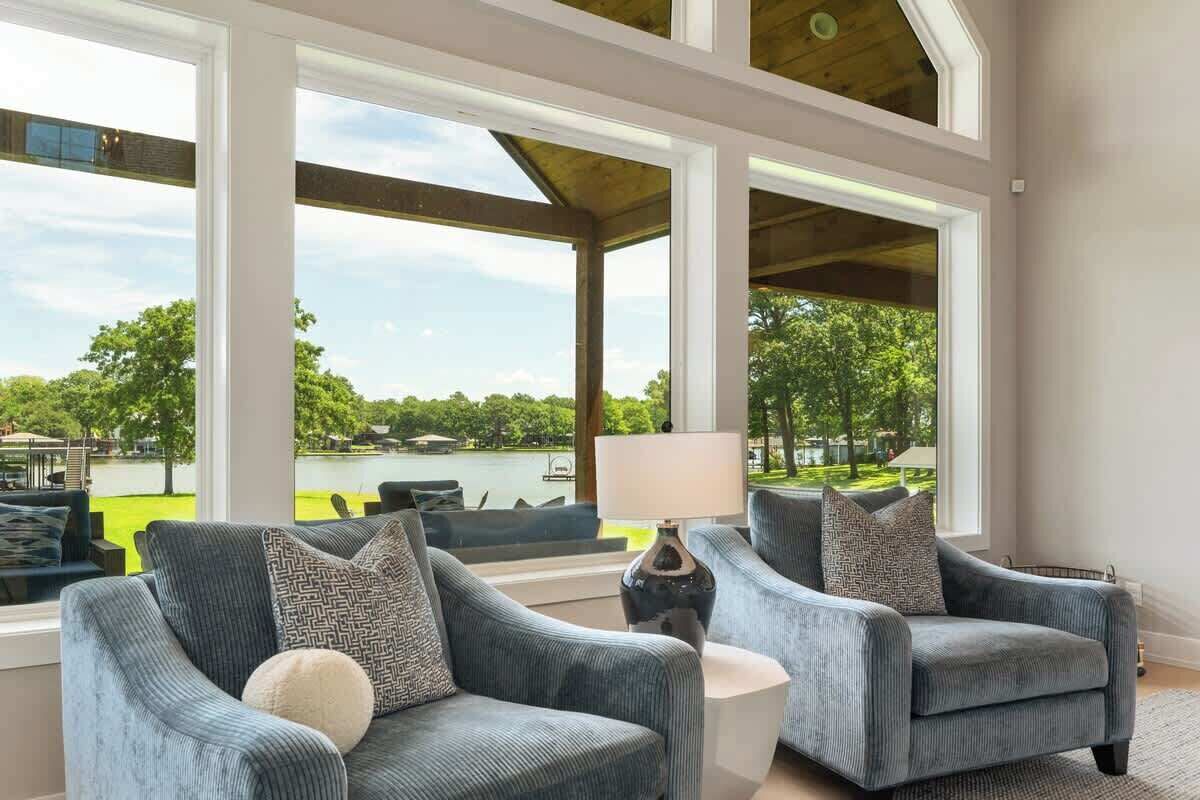A room with two armchairs, a small table, and large windows offering a view of a lake and greenery.