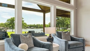 Una habitación con dos sillones, una mesita y amplias ventanas que ofrecen vistas a un lago y vegetación.