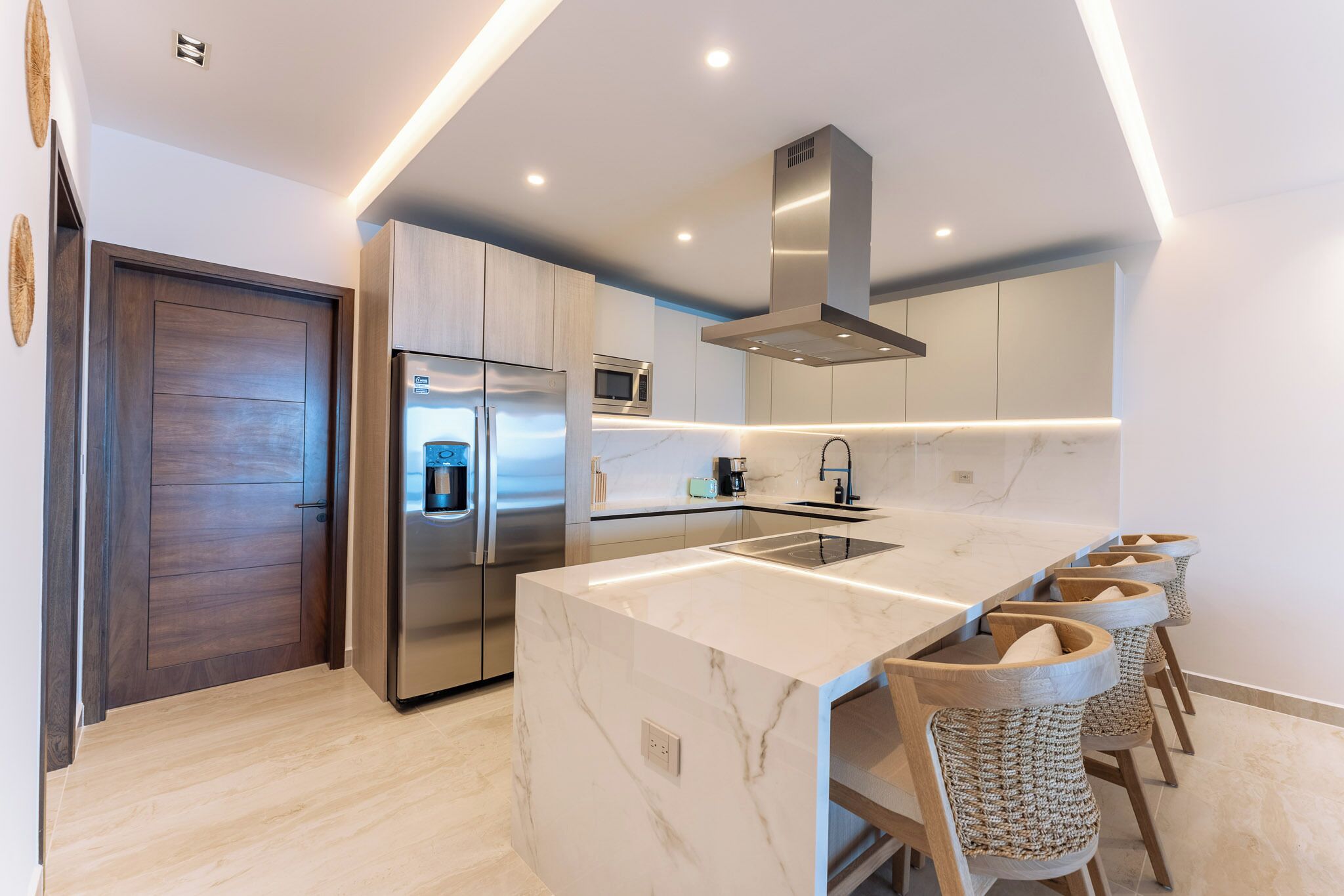 A modern kitchen with a marble island, stainless steel appliances, and bar stools.