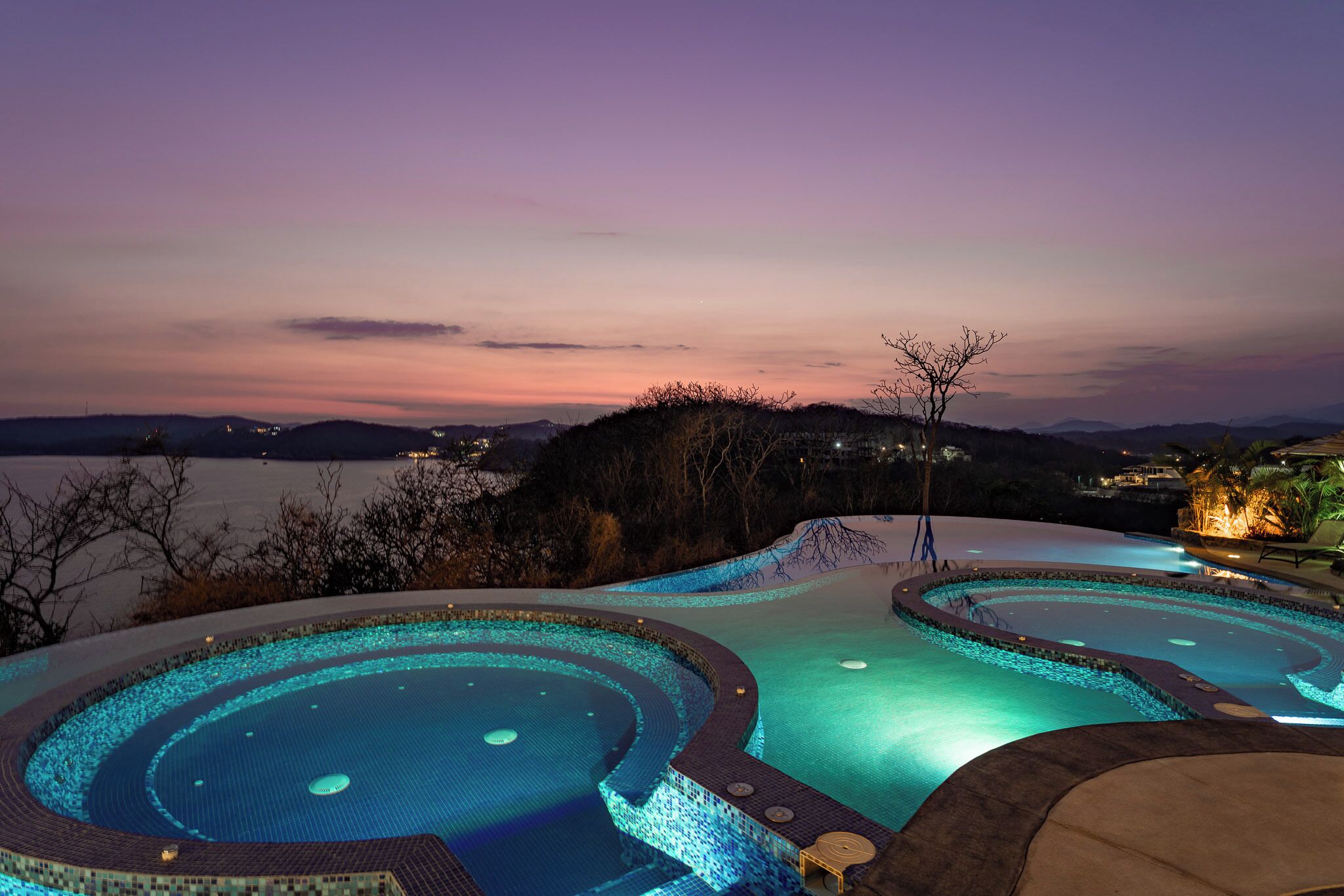 A pool area with a view of the water body and distant hills.