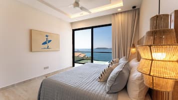 A modern bedroom with a large bed, a ceiling fan, a view of the sea, and a beachside balcony.