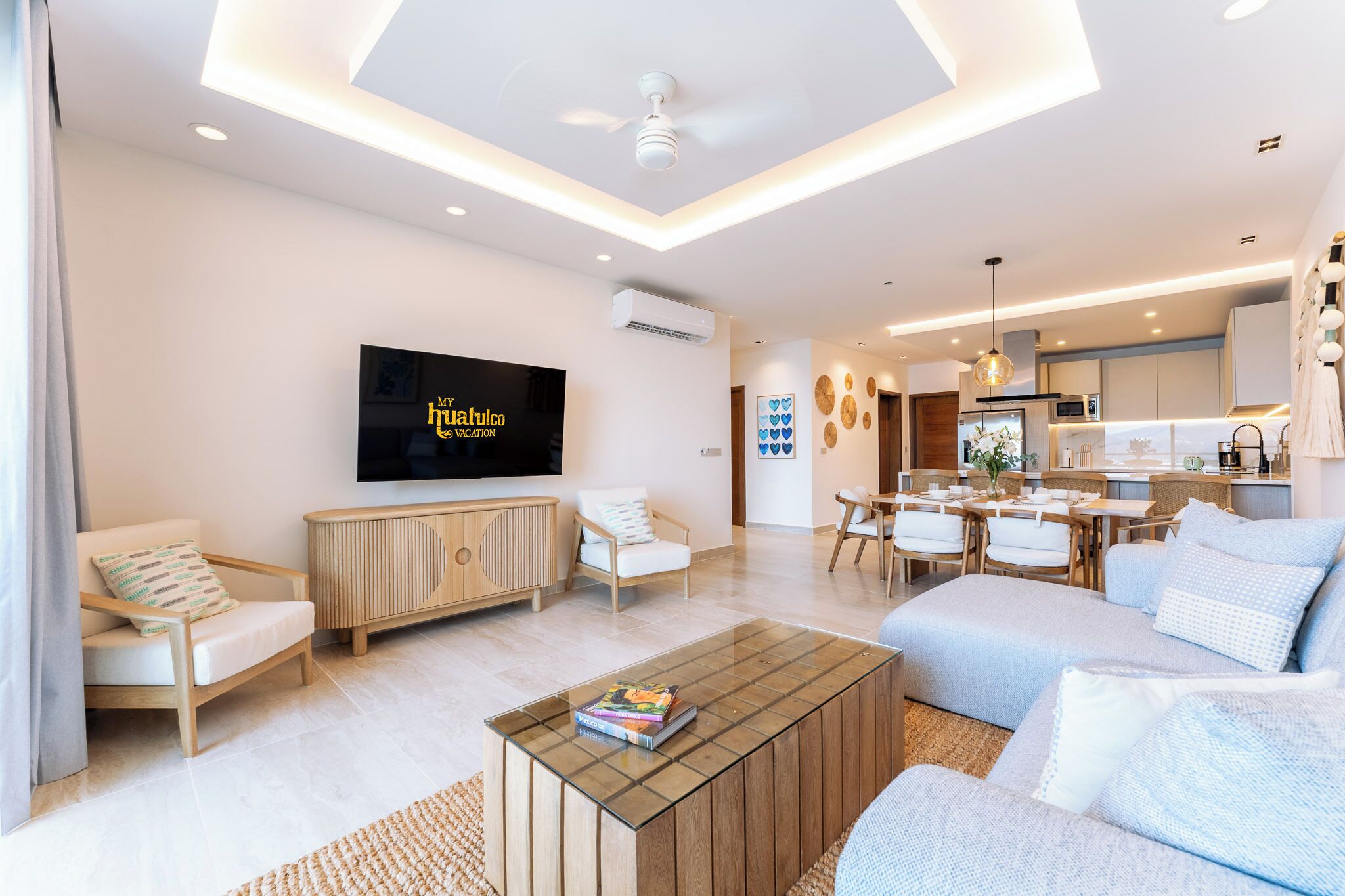 A modern living room with a flat-screen TV, a dining area, and a kitchen.