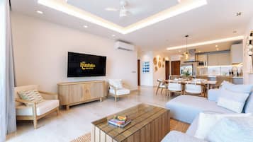 A modern living room with a flat-screen TV, a dining area, and a kitchen.