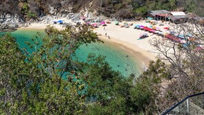 Een strand met helder turquoise water, een zandstrand en diverse kleurrijke parasols.