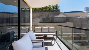 Een modern balkon met een bank en stoelen, een glazen balustrade en uitzicht op een rotsachtig landschap.