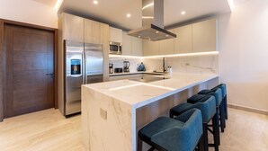 Een moderne keuken met een groot eiland, roestvrijstalen apparatuur en barstoelen.