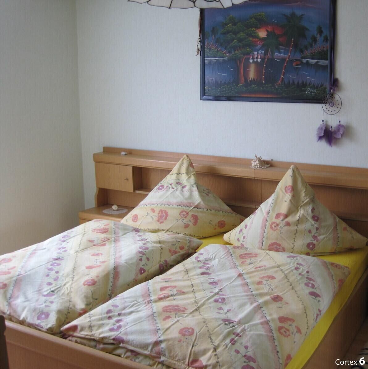 Camera da letto con due letti, una testiera in legno, un comodino e un quadro appeso al muro.