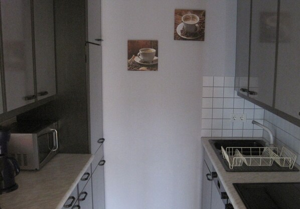 Una cocina compacta con microondas, lavamanos y alacena.