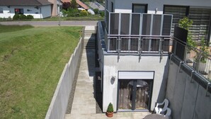 A residential building with a balcony, a small garden, and a paved pathway leading to the entrance.