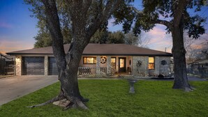A two-story stone house with a garage, surrounded by well-maintained grass and large trees. - Dean's Retreat At Georgetown 3 Bedroom Home (Georgetown)