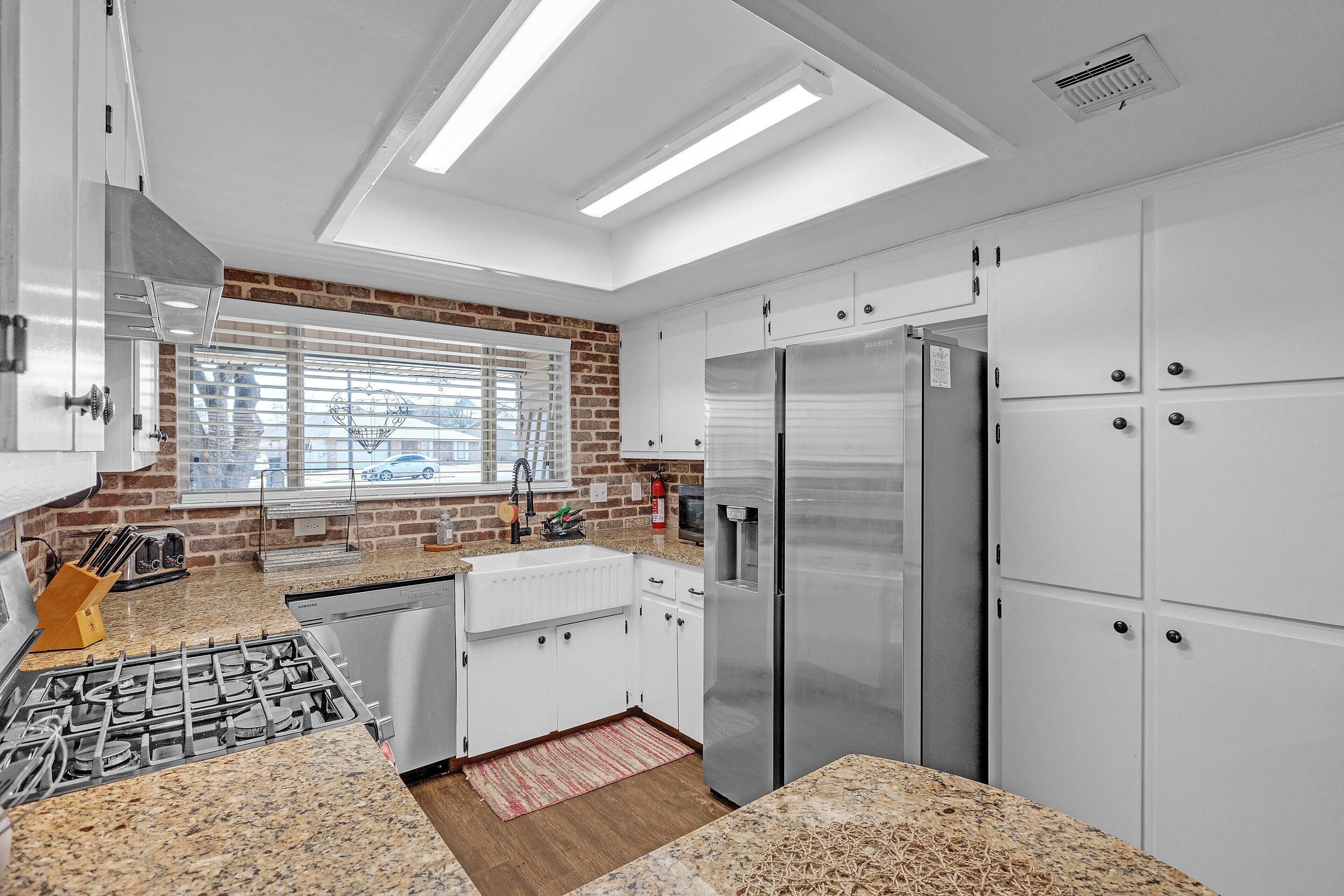 A modern kitchen with white cabinets, stainless steel appliances, and a brick accent wall.